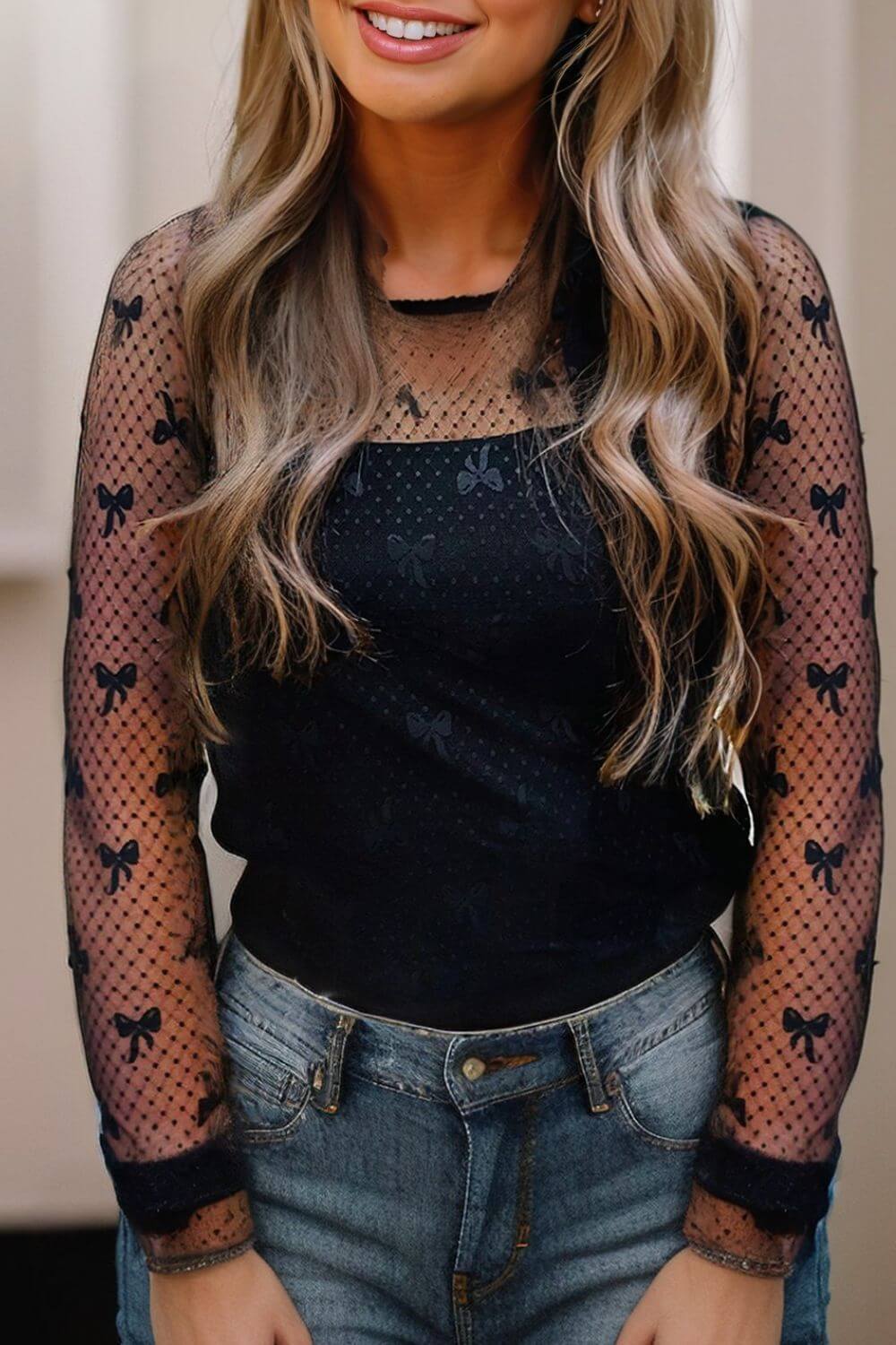 Model wearing a black sheer top with bow patterns, styled with jeans, showcasing a chic and playful look.